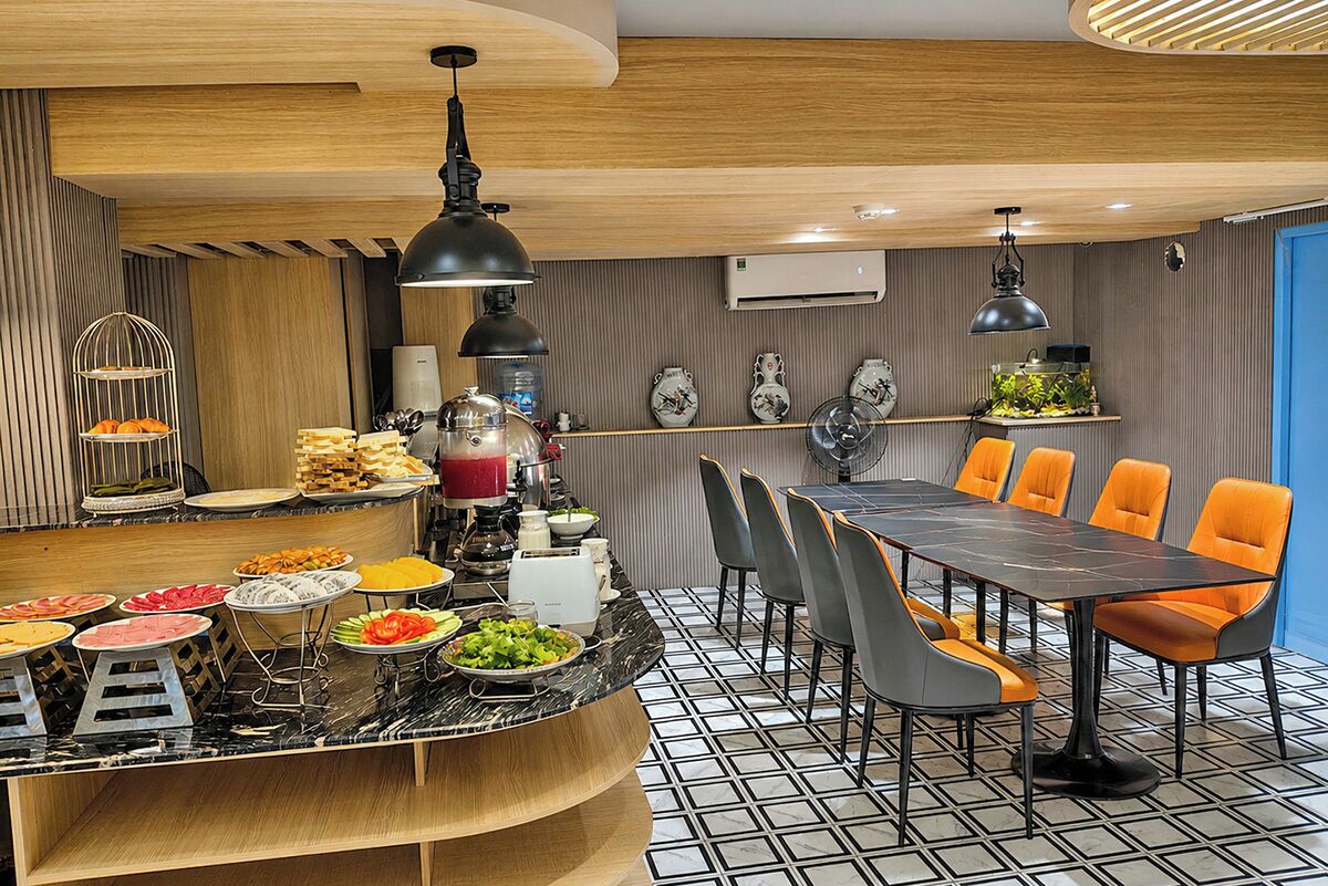 A modern dining area with a marble countertop, buffet, and a long table with orange chairs.