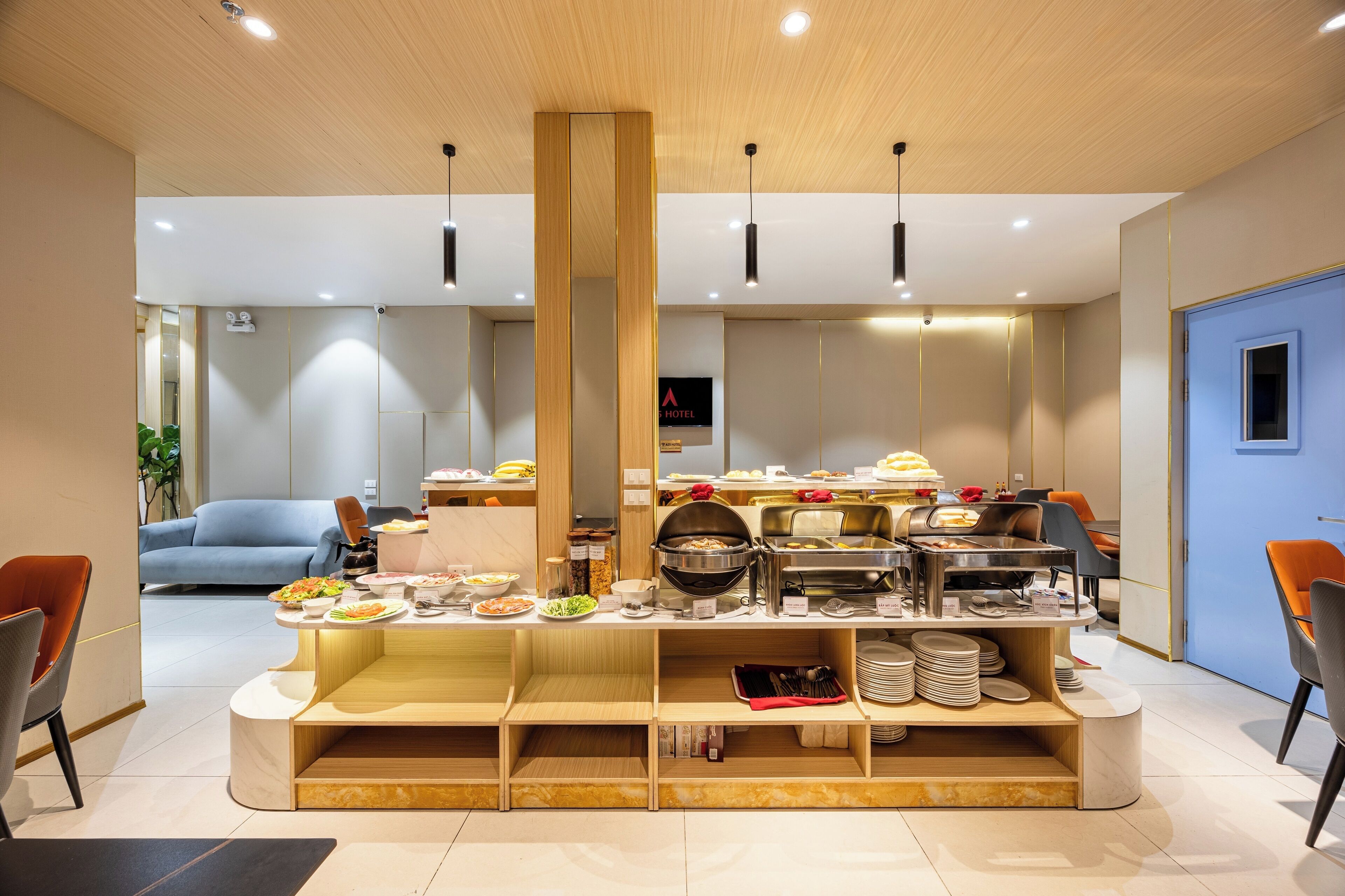 Et moderne hotelmorgenmadsområde med en central buffet, siddepladser og en blå dør.