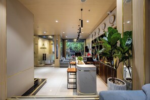 Een moderne hotellobby met een receptiebalie, een zithoek en uitzicht op buiten.