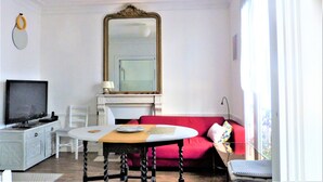 Una sala de estar con televisor, una mesa con un plato, un sofá rojo y un espejo grande.