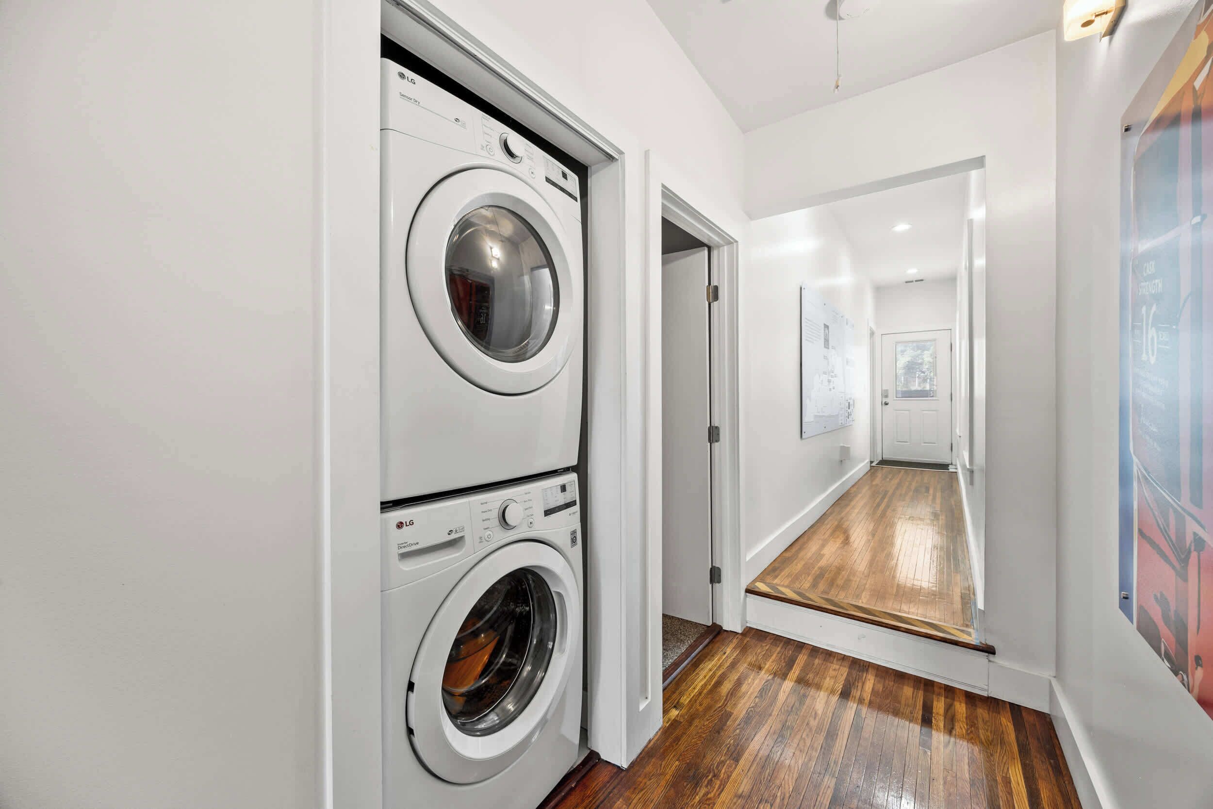 A laundry room with two stacked washing machines and a wooden floor.