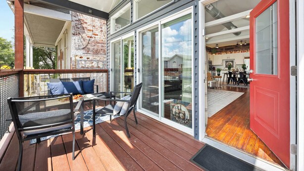 Een terras met buitenmeubilair, een rode deur en uitzicht op een keuken.