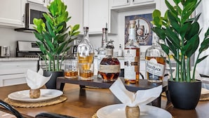 Een keuken met witte kastjes, een magnetron, en een tafel met whiskyflessen en potplanten.