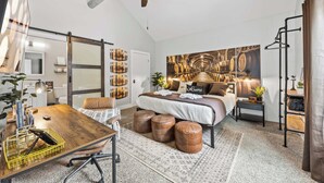 Een slaapkamer met een bed, een bureau, een stoel, een plafondventilator en een groot muurdecoratie.