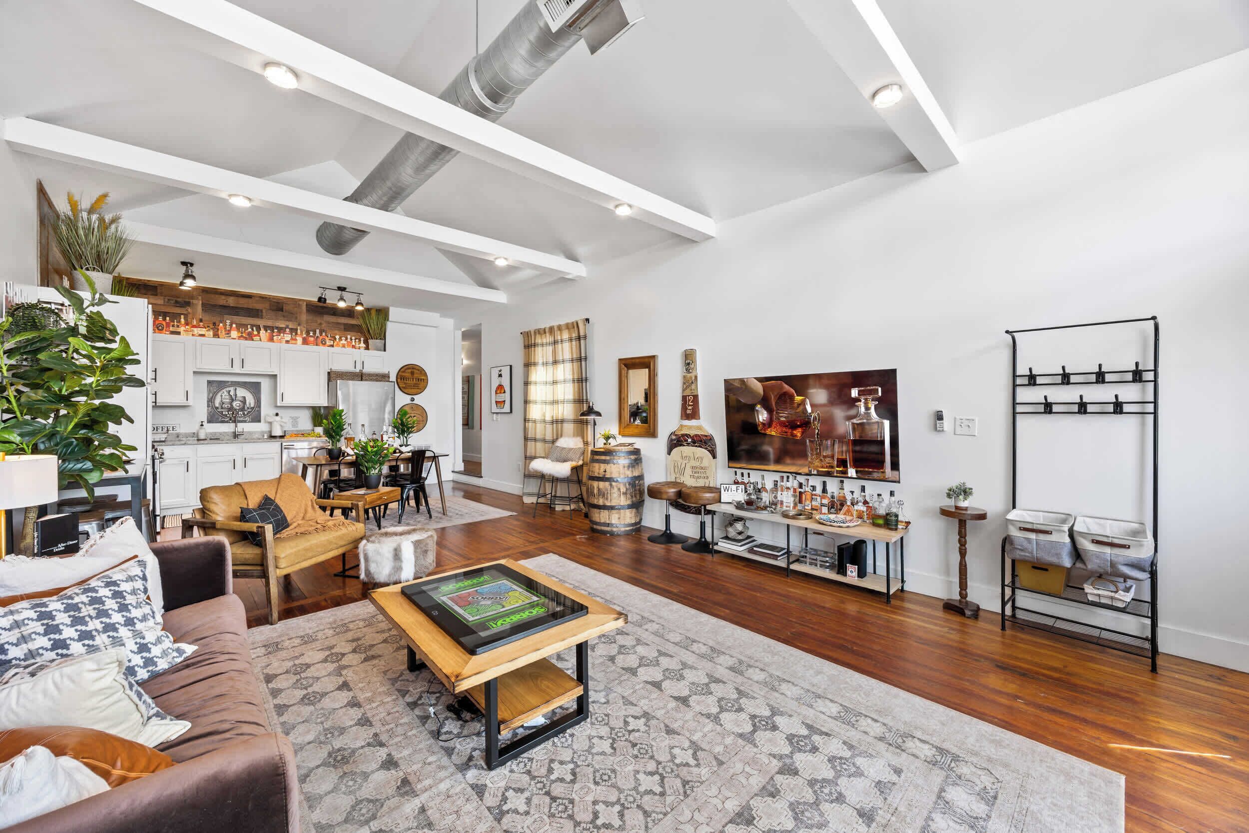 A spacious living area with a wooden floor, a brown leather sofa, a coffee table, and a dining area with a wooden table and chairs.