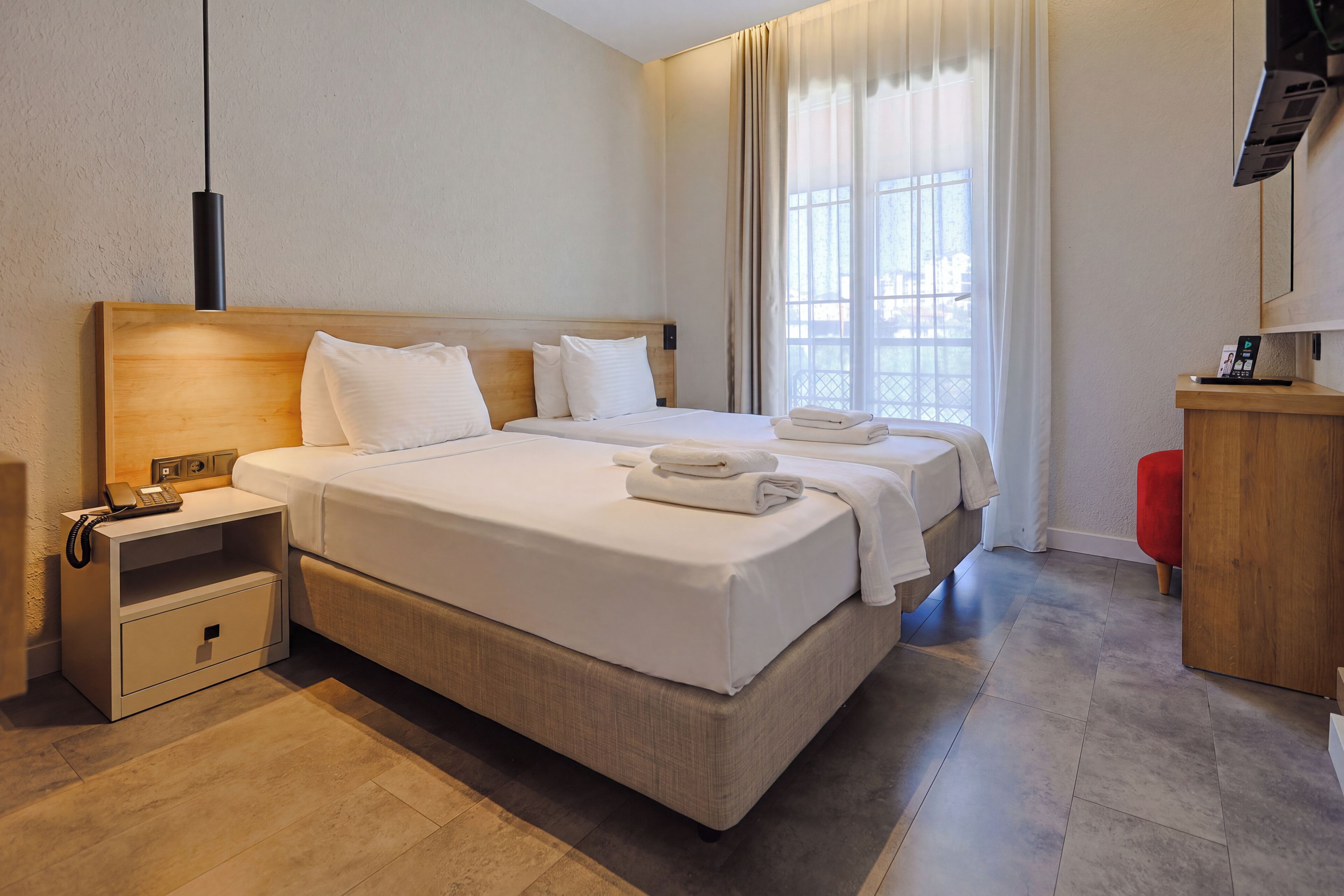 A hotel room with a large bed, bedside tables, a desk with a telephone, and a television on the wall.