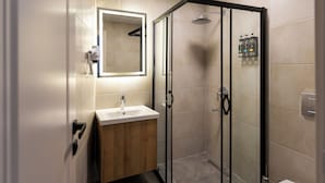 Een moderne badkamer met een douchecabine van glas, een houten wastafelmeubel en een witte wasbak.