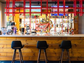 A bar area with stools, a counter with various bottles, and a red neon sign.