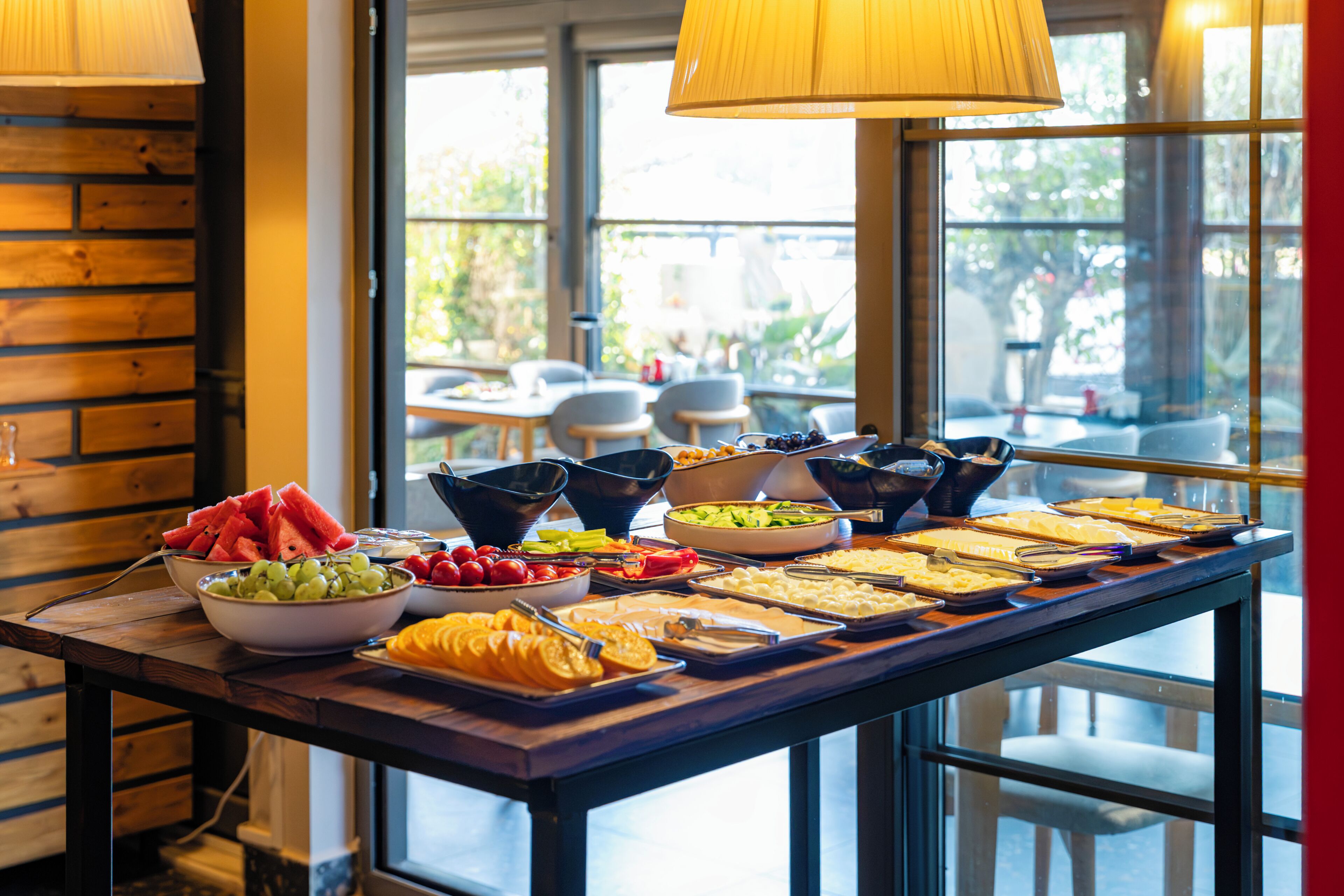 A buffet table with various food items and a window view.