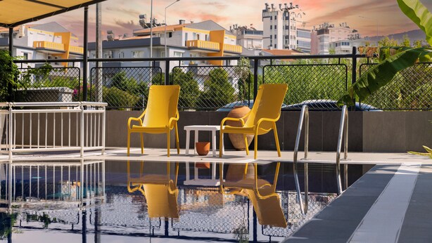 A rooftop pool area with yellow chairs and a table, surrounded by a metal fence and overlooking a cityscape. - 7 inn  (Konyaalti)