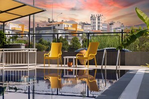 A rooftop pool area with yellow chairs and a table, surrounded by a metal fence and overlooking a cityscape. - 7 inn  (Konyaalti)