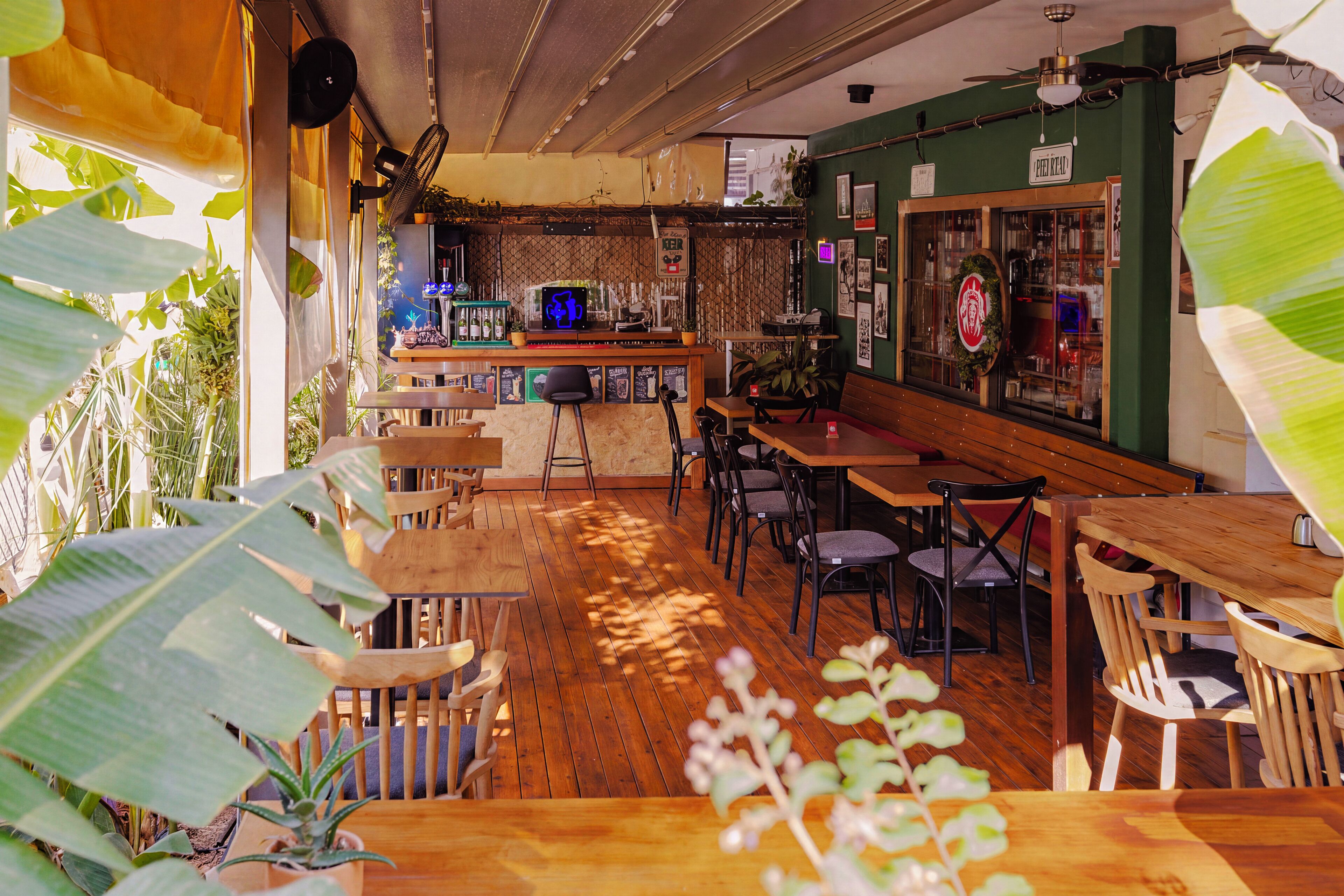 A restaurant interior with wooden tables and chairs, a bar area, and various plants.