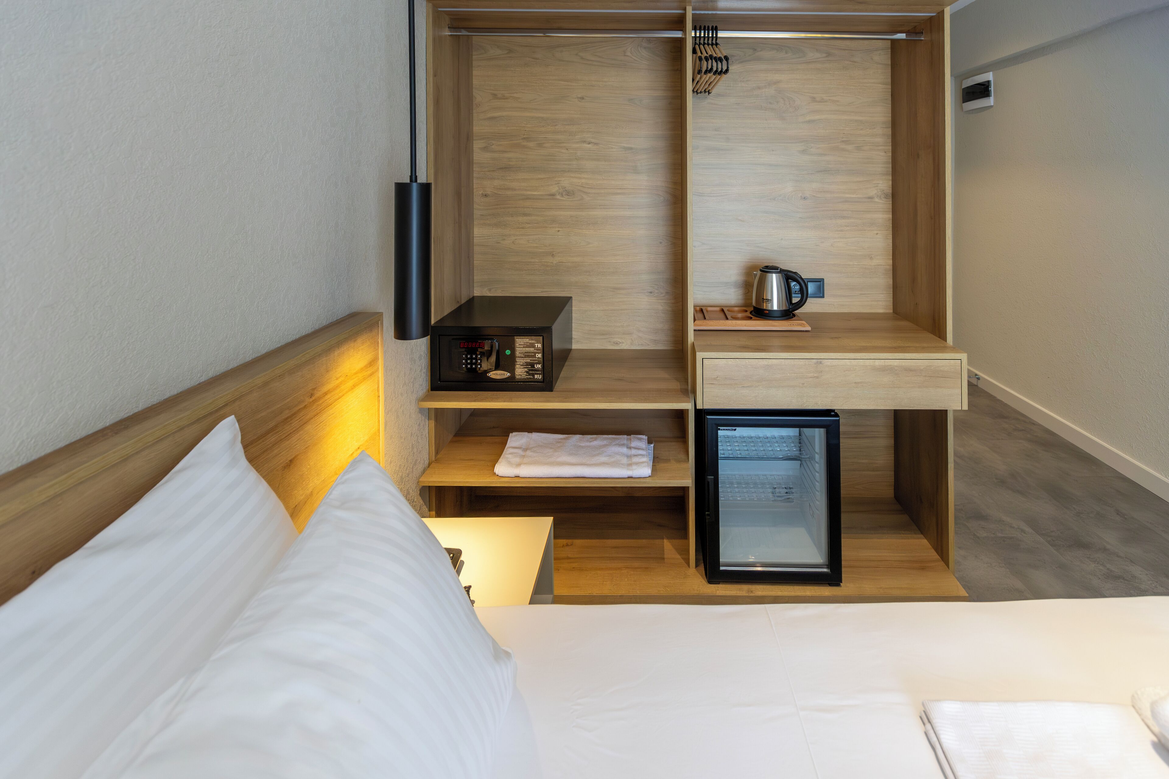 Habitación de hotel compacta con cama, un escritorio pequeño, un mini refrigerador, hervidor de agua y microondas.