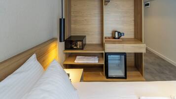 Habitación de hotel compacta con cama, un escritorio pequeño, un mini refrigerador, hervidor de agua y microondas.