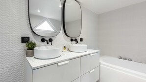 A modern bathroom with two large oval mirrors, a white bathtub, and a marble countertop. - Résidence Paris Charles (Paris)
