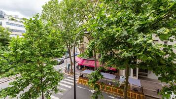 Straßenansicht mit Café unter einem Baum, Fußgängerüberweg und einem Gebäude mit pinkfarbenem Vordach.
