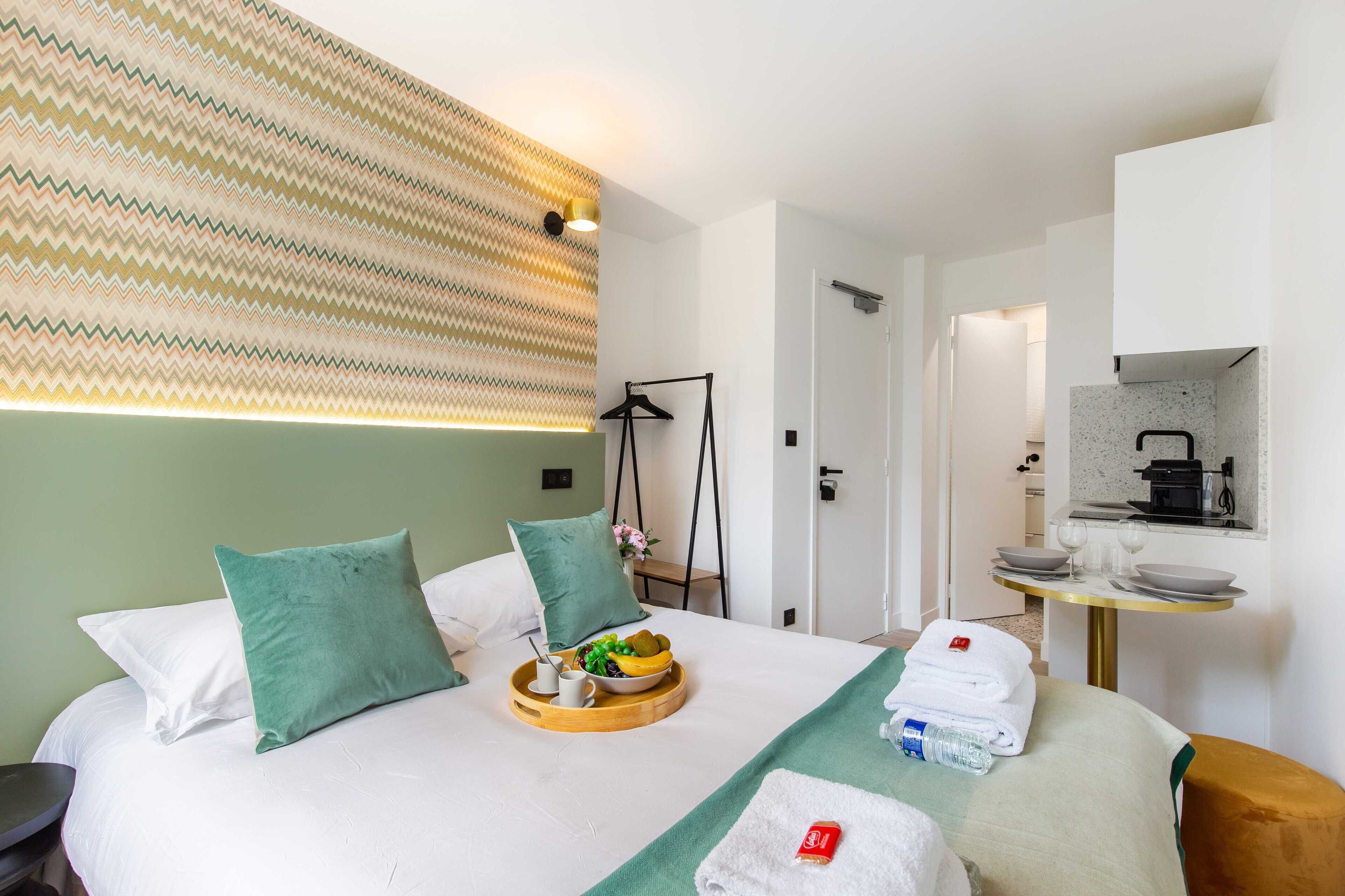 A hotel room with a bed, a breakfast tray, towels, and a small table with a kettle and glasses.