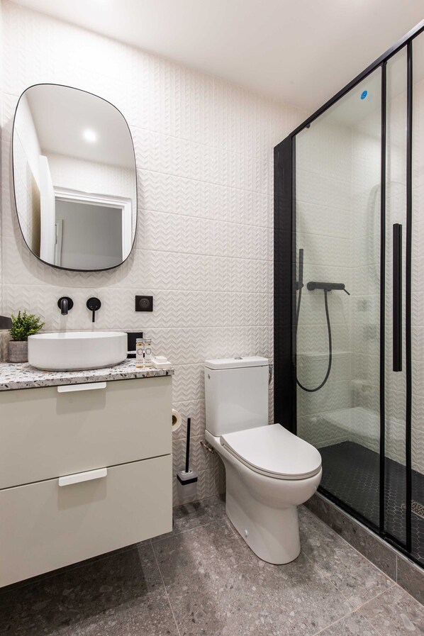 A modern bathroom with a white sink, a toilet, and a glass-enclosed shower. - Résidence Paris Charles (Paris)