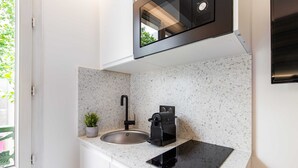 A compact kitchen with a stainless steel sink, a small potted plant, a coffee machine, and a microwave. - Résidence Paris Charles (Paris)