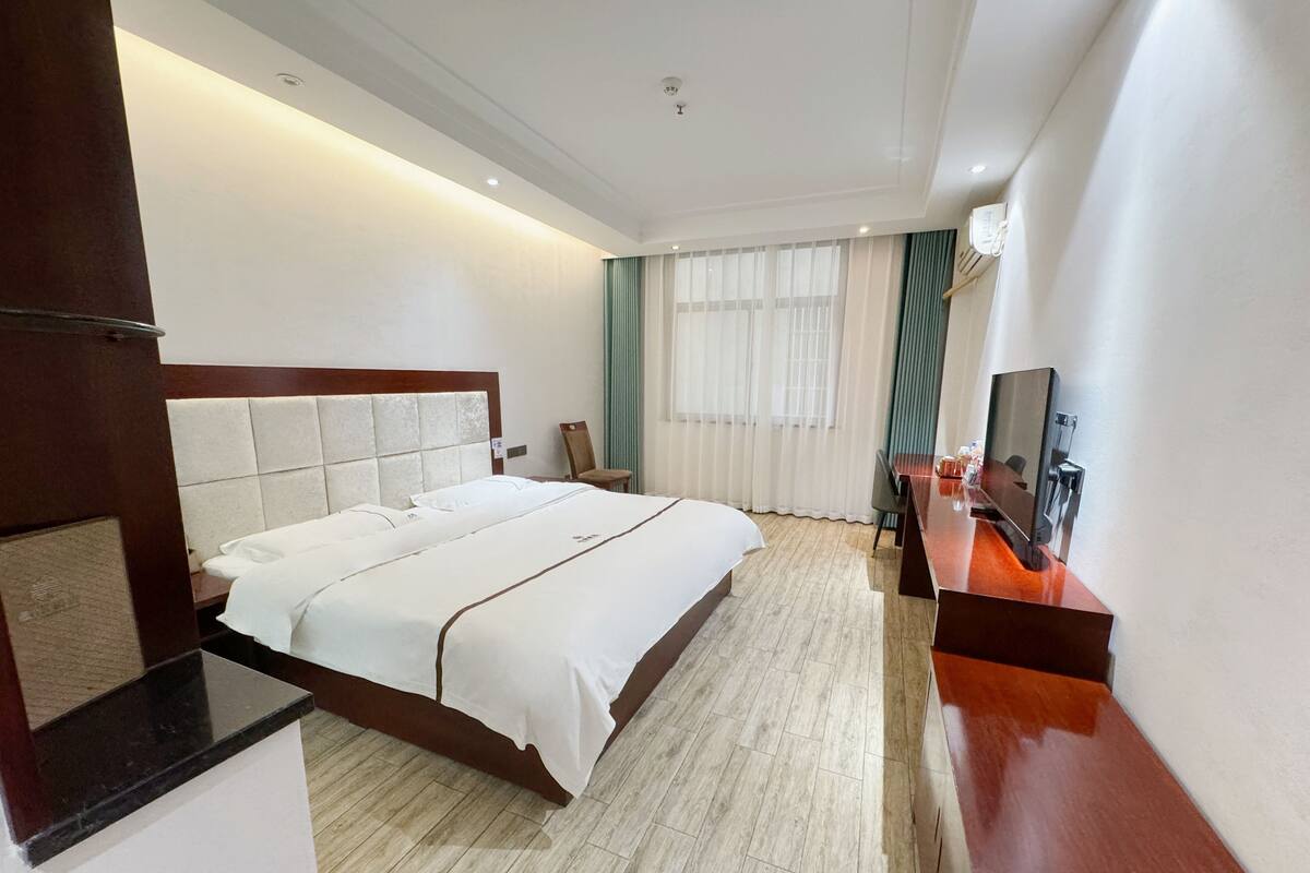A hotel room with a large bed, a desk, a chair, and a television.