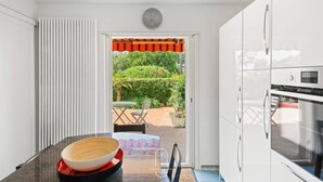 A modern kitchen with a view of a garden through an open door. - Charmant RDJ T3 en bord de mer Carqueiranne (CARQUEIRANNE)