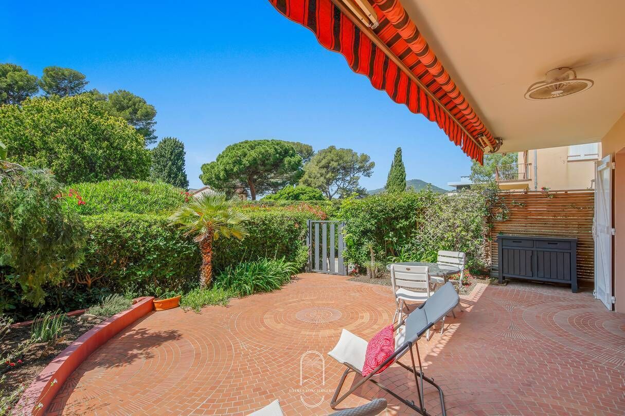 Une terrasse avec un sol en briques, des sièges extérieurs et une vue sur un jardin agrémenté d’arbres et d’arbustes.