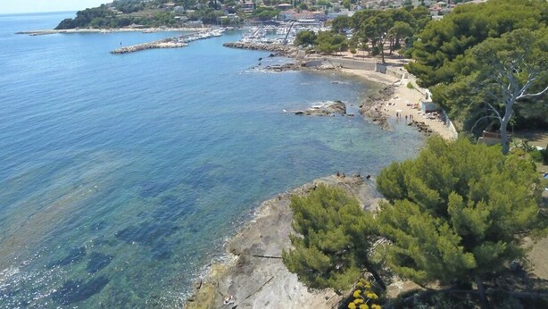 A coastal town with clear blue waters, rocky shores, and a mountainous backdrop. - Charmant RDJ T3 en bord de mer Carqueiranne (CARQUEIRANNE)