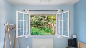 A bedroom with an open window, a bed, a radiator, and a nightstand with a lamp. - Charmant RDJ T3 en bord de mer Carqueiranne (CARQUEIRANNE)