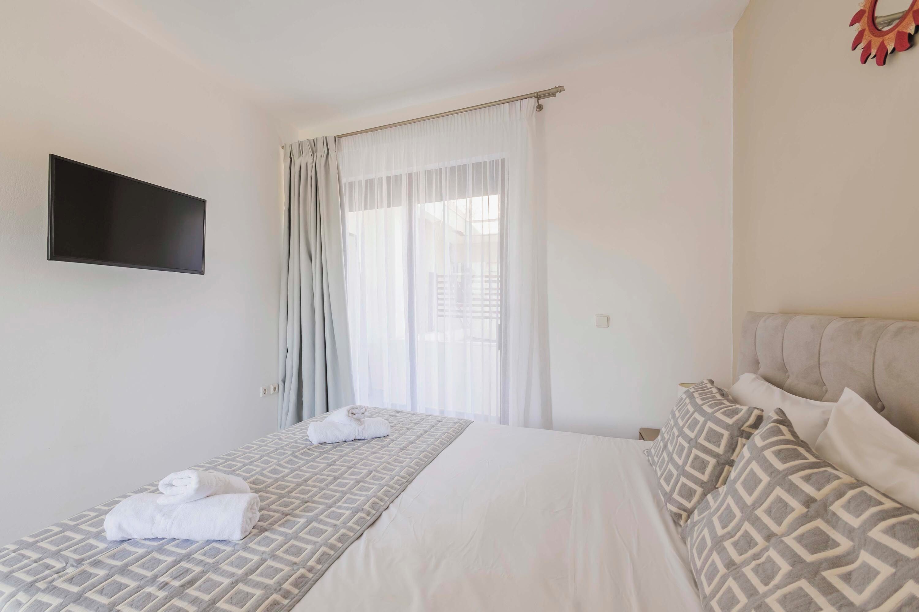 A hotel room with a bed, a TV mounted on the wall, and a window with curtains.