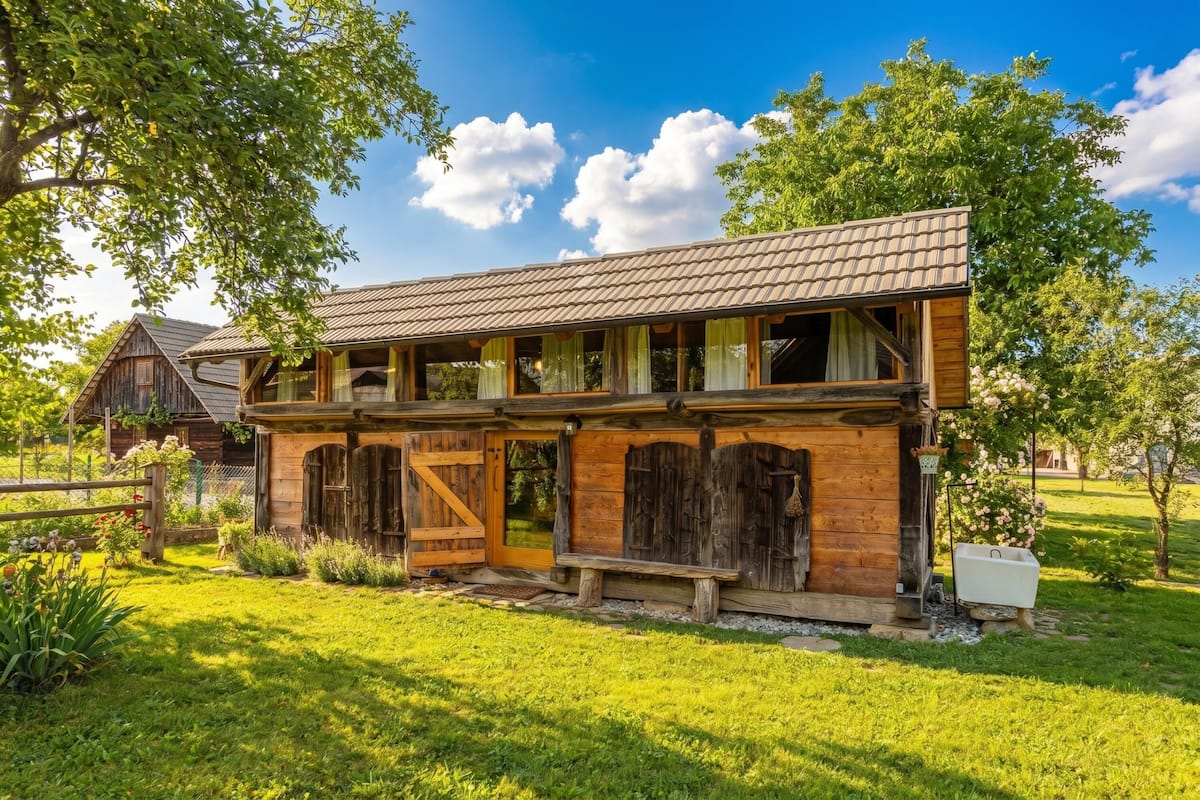 A rustic wooden house with a porch, a large wooden door, and a small garden area.