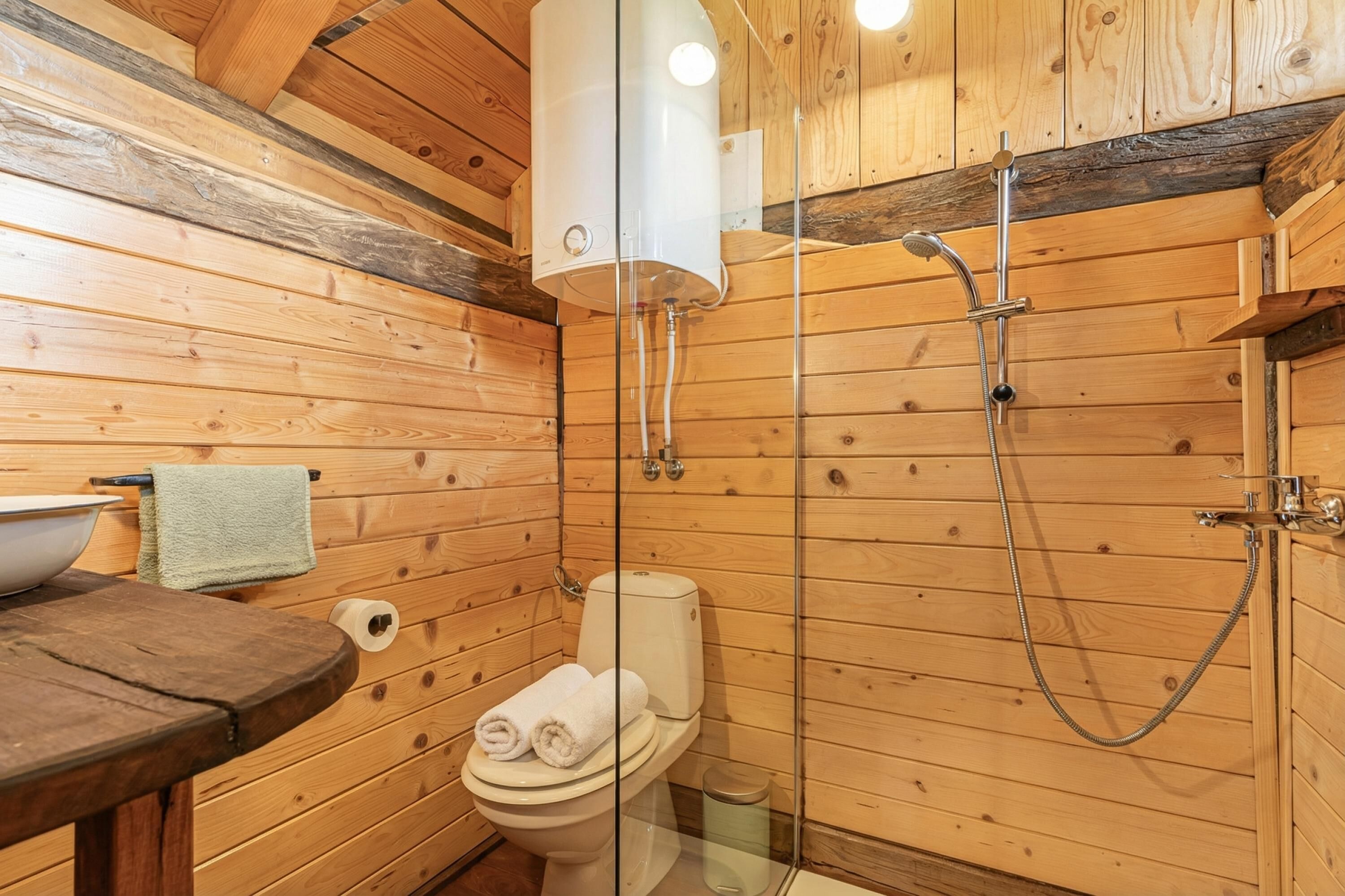 A wooden cabin bathroom with a toilet, a glass-enclosed shower, and a wooden table with a bowl.