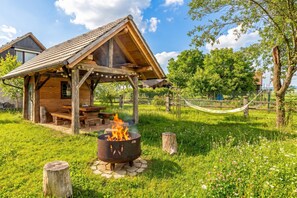 A rustic wooden cabin with a fire pit, a hammock, and a grassy area.