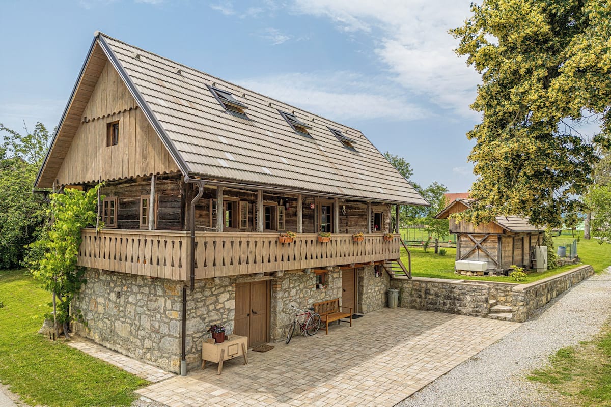 A rustic wooden building with a stone foundation, a balcony, and a bicycle parked outside.