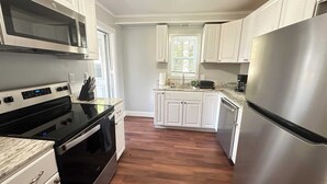 A modern kitchen with white cabinets, stainless steel appliances, and a wooden floor. - Strikeout - All Star Baseball Rentals (Oneonta)