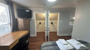 A bedroom with a bed, a desk, a chair, a TV, and a walk-in closet. - Strikeout - All Star Baseball Rentals (Oneonta)