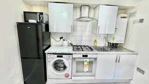 Une cuisine compacte avec un réfrigérateur noir, un lave-linge encastré, une cuisinière et un évier.