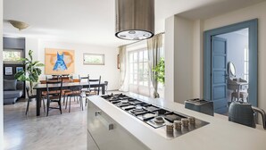 Una cuina moderna amb una illa central, zona de menjador i una porta blava que dona a un bany.