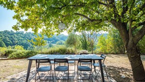 Zona d'exterior per dinar amb taula i cadires sota un arbre, en un entorn natural.