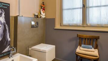 A bathroom with a white sink, a wooden chair, and a window with frosted glass.