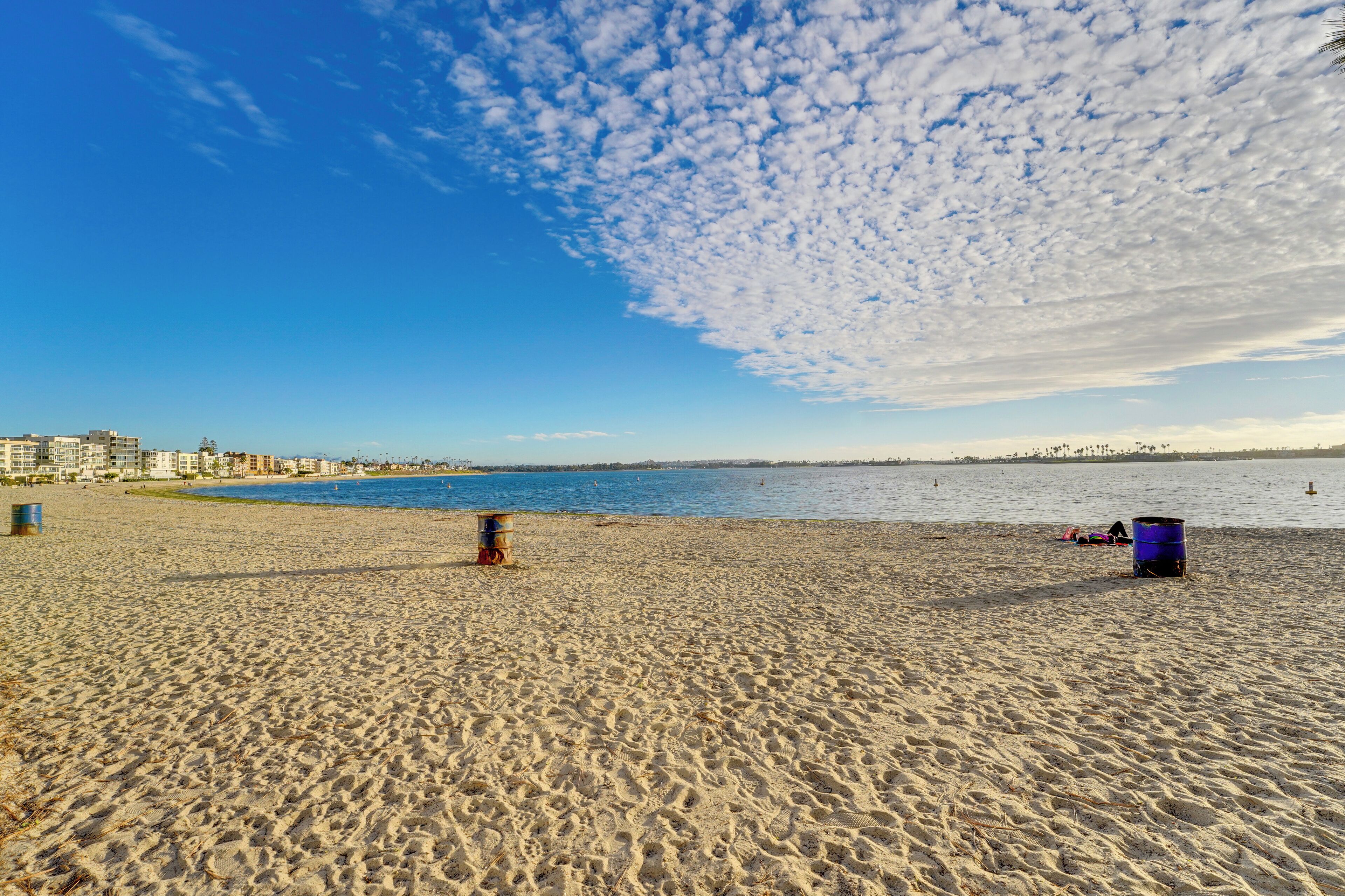 A wide sandy beach with a clear blue sky and scattered clouds.