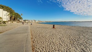 A beach with a concrete walkway, a palm tree, and a building in the background.