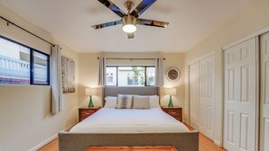 A bedroom with a bed, bedside tables, a ceiling fan, a window, and a door.