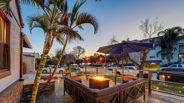 An outdoor patio with a fire pit, seating, and palm trees.