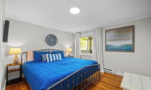 A bedroom with a bed, two bedside tables, a wall clock, a round wall decoration, a window with curtains, and a painting on the wall.