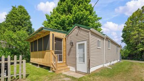 A small, single-story house with a screened porch and a garage. - Short Description: Lakewood Bungalow | Screened Porch • 2 Baths • Basement Hangout • Walk to Lake• Onsite Laundry (Coloma charter Township)