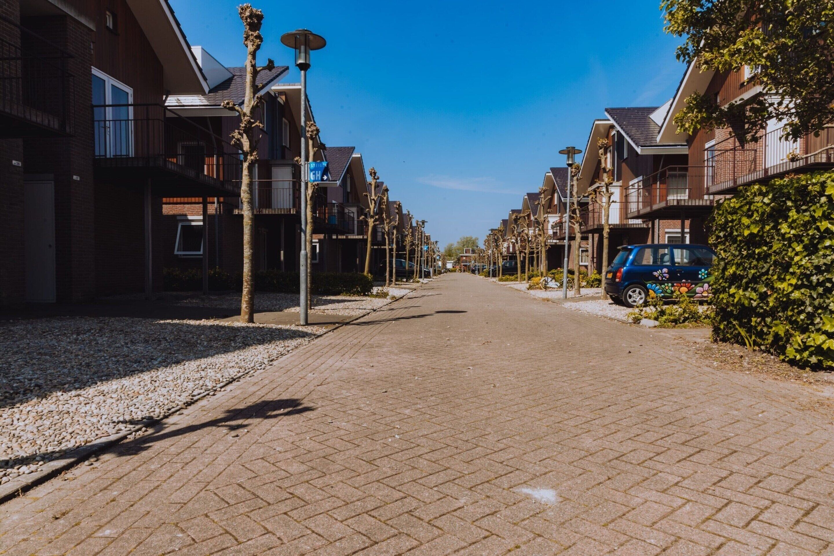 A residential street with houses on both sides, a paved walkway, and a parked car.