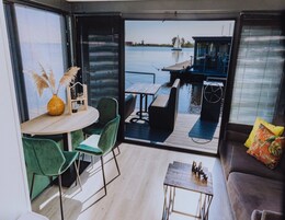 A modern interior with a dining area, a sofa, and a view of a water body with a dock.