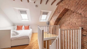 A bedroom with a loft bed, white walls, wooden beams, brick wall, and two skylights. - Cosy 2-Bed Cottage, close to Windsor By Tempstay (Berkshire)