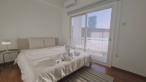 Een slaapkamer met een bed, nachtkastje, lamp en uitzicht op buiten door een schuifdeur.
