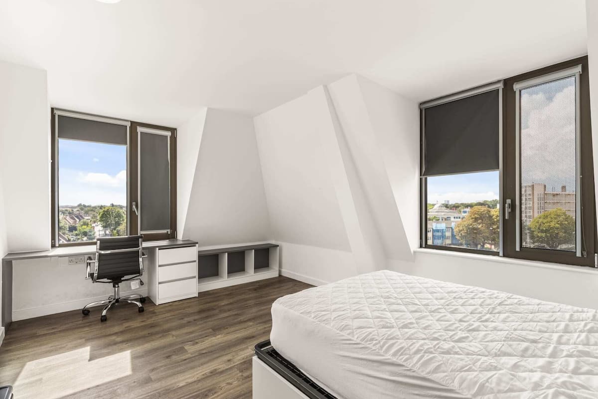 Ein Schlafzimmer mit Bett, Schreibtisch, Stuhl und großen Fenstern.